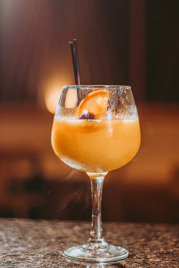 Close-up of a vibrant orange cocktail with a fruit slice and straw in a glass, perfect for summer vibes.