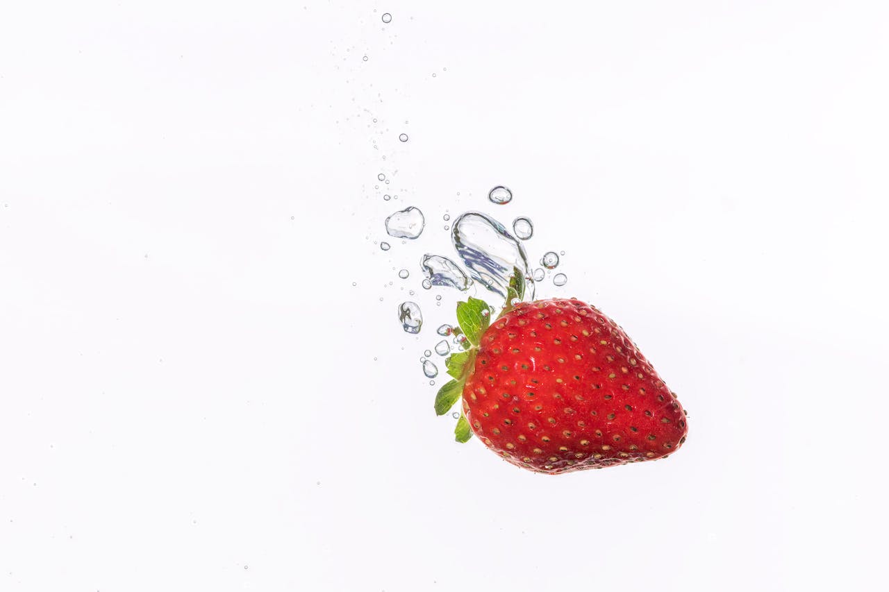 A vibrant strawberry making a splash in clear water, captured in mid-air with perfect clarity.