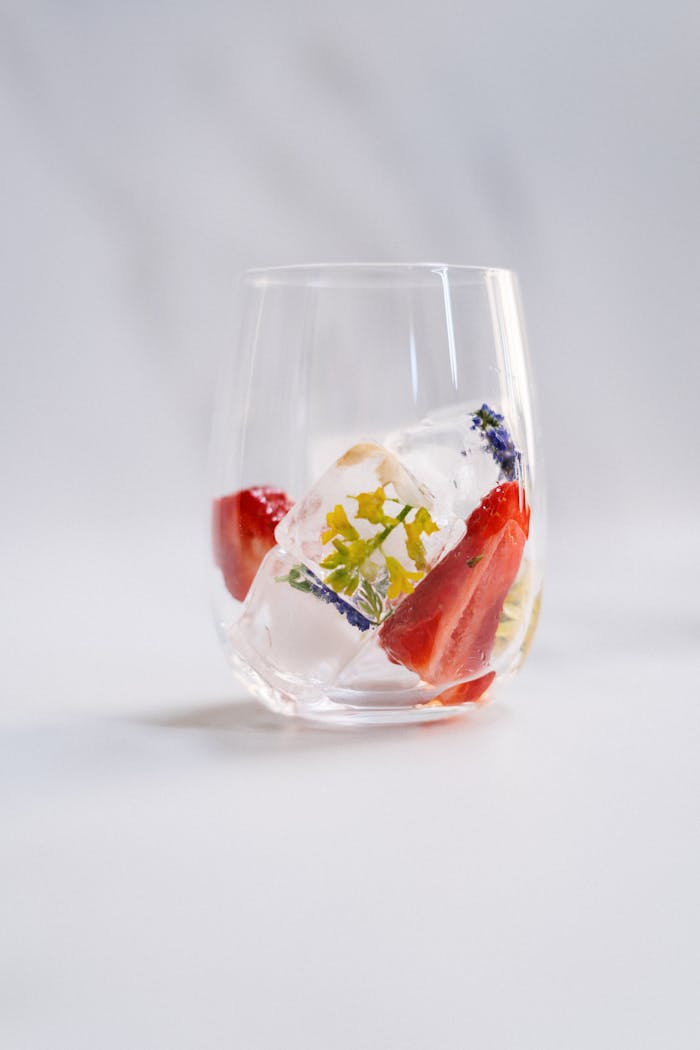 A glass with decorative ice cubes featuring strawberries and flower petals, perfect for a vibrant cocktail.