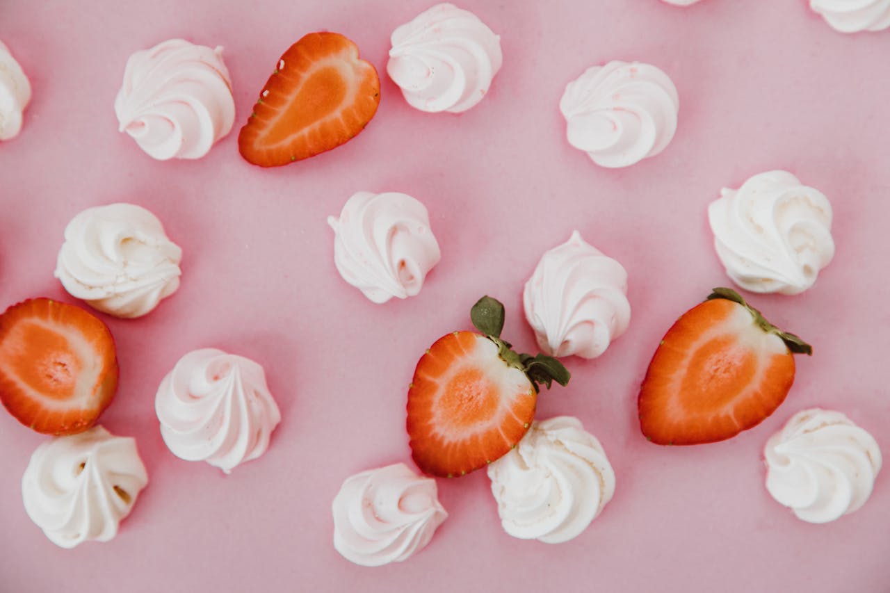 Close-up of sliced strawberries and meringue swirls on a pink background.