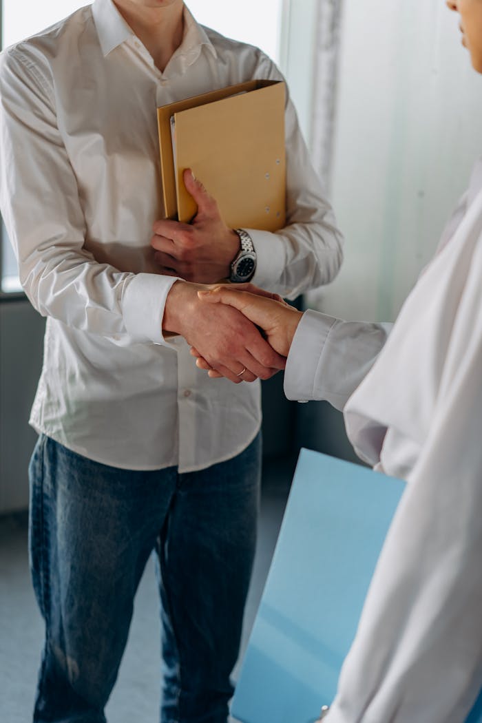 Two colleagues in casual office attire shaking hands, symbolizing a professional agreement.